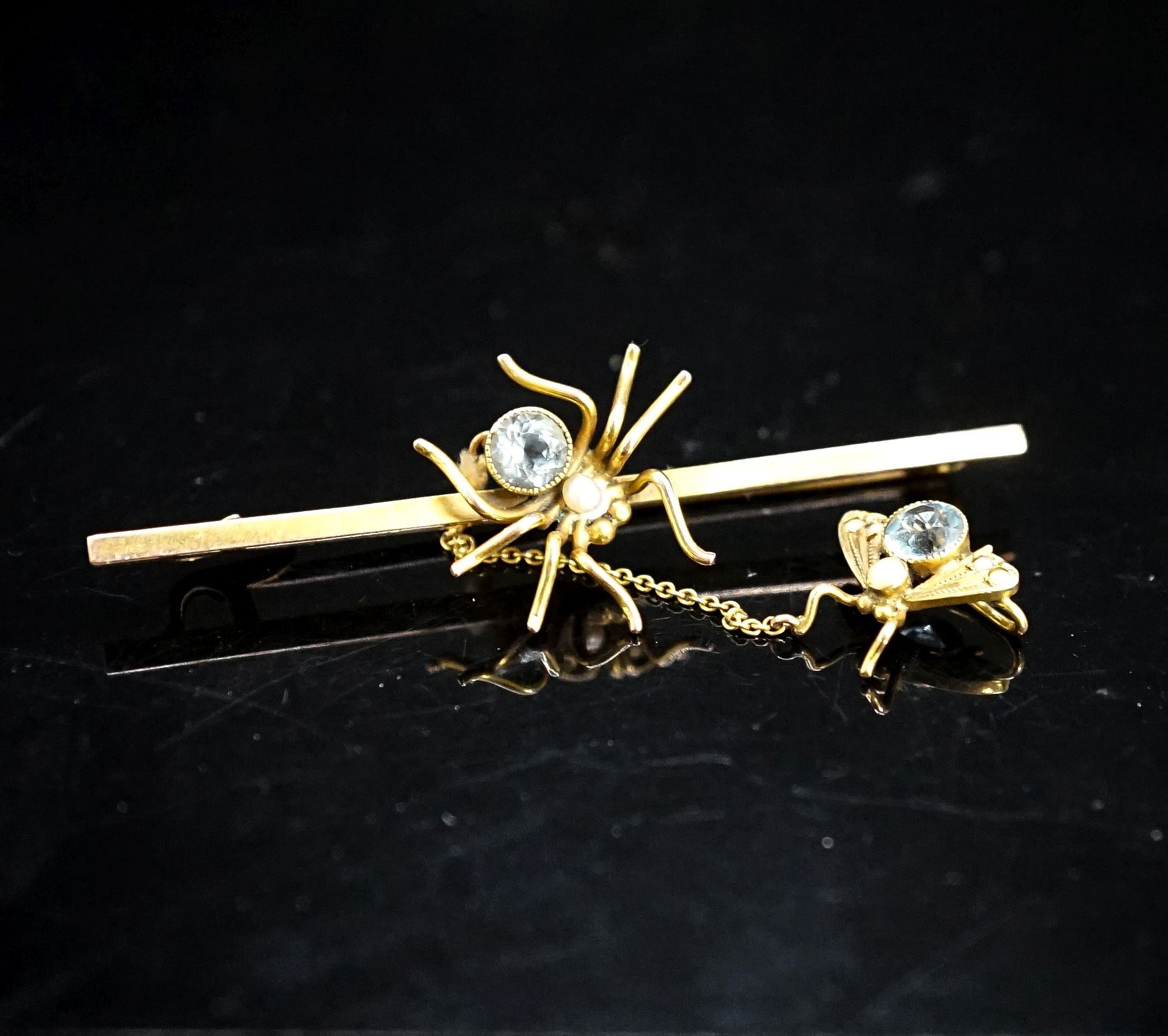 An Edwardian yellow metal and gem set spider bar brooch, 53mm, the safety chain with similar gem set fly, gross 2.8 grams.